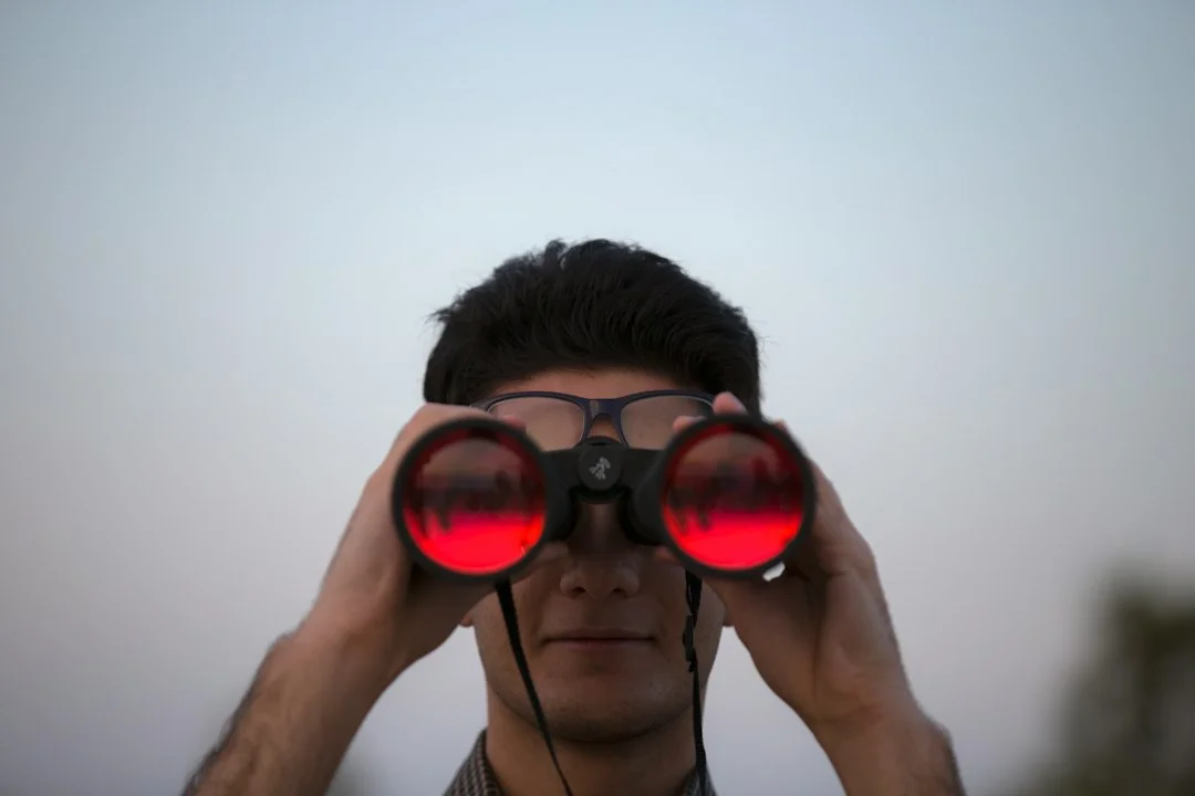 Uma pessoa usando binóculos para observar o céu noturno, uma dica prática de como observar planetas juntos.